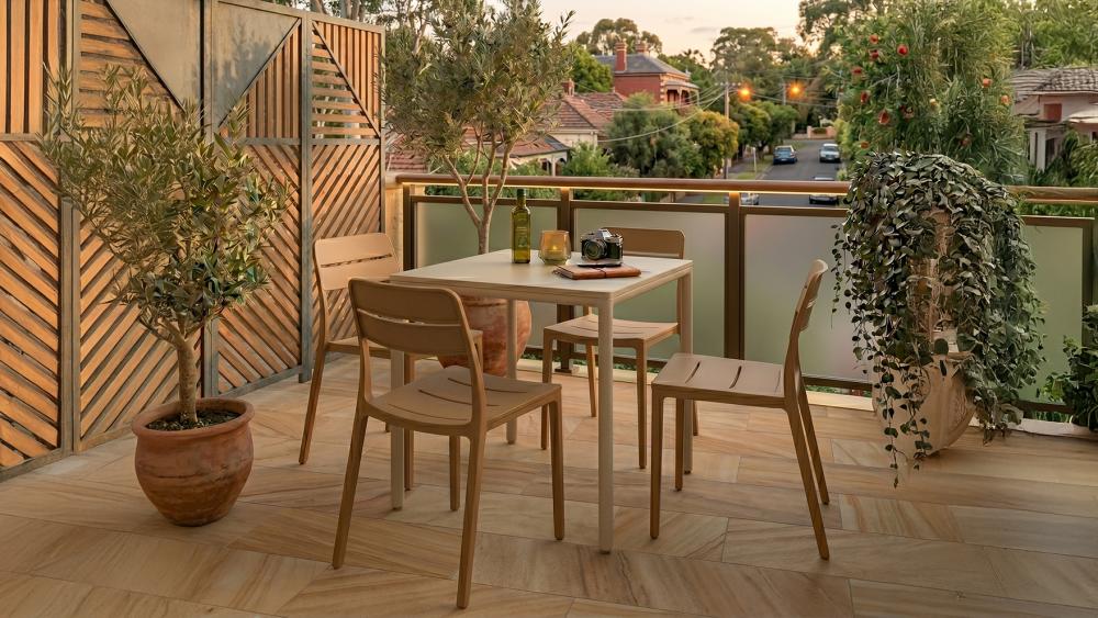 Two compact lounge chairs and a side table on a west-facing apartment balcony at sunset