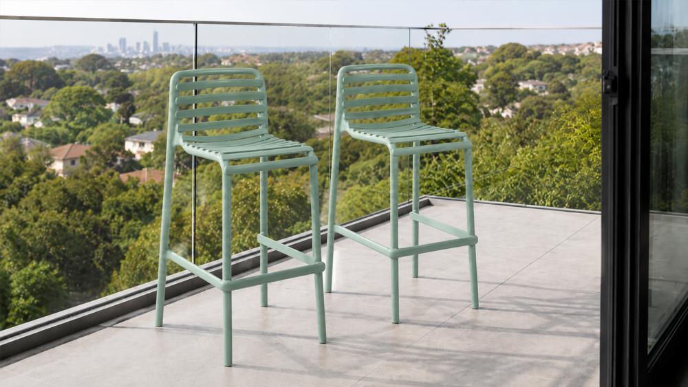 Slim two-stool outdoor bar setting positioned against a balcony rail in a compact apartment space