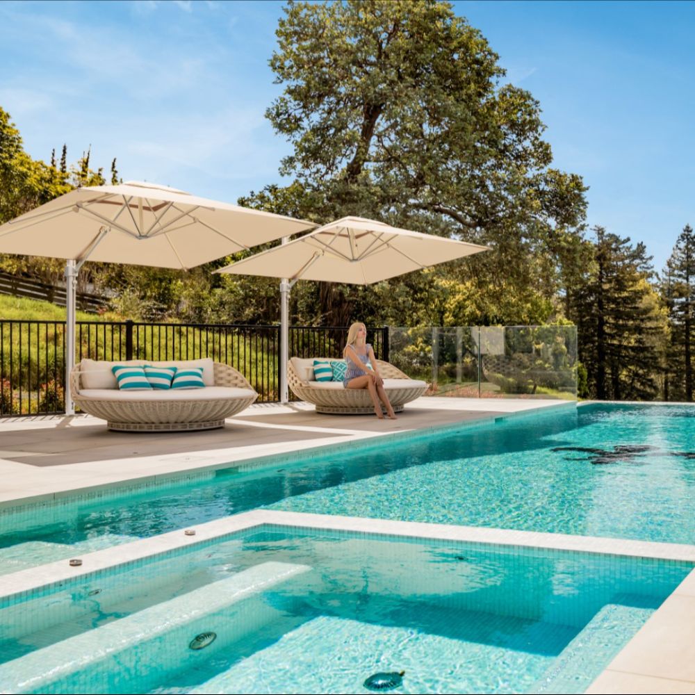 Two Eclipse V4 3m square cantilever umbrellas with aluminium masts shading outdoor daybeds beside a swimming pool
